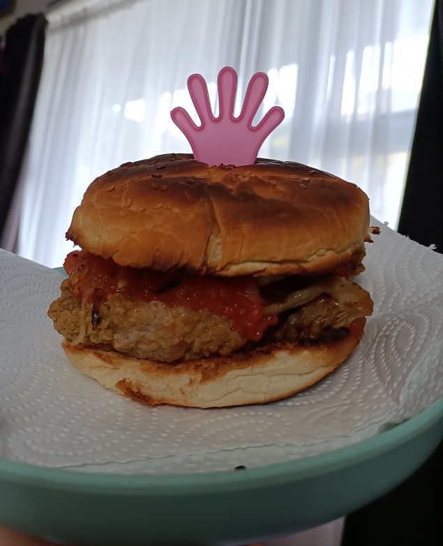 Home grilled chicken burger with oyster mushrooms and tomato sitting on plate, with pink hand-shaped stick thing poking out the top. Yum!